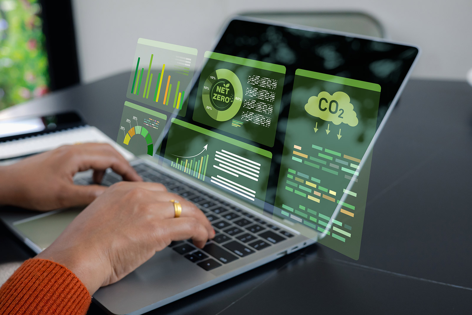 Hands typing on a laptop with glowing screens showing charts and a CO2 cloud icon.